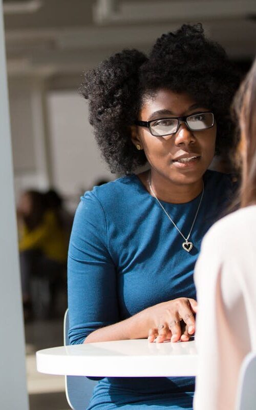 Two women engaged in a discussion in a modern office environment, highlighting communication and interaction.