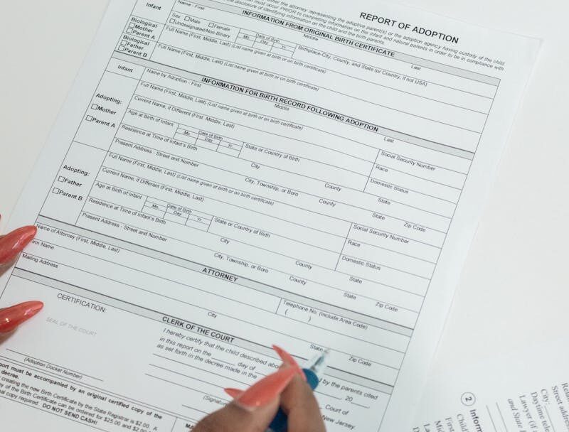 A woman with red nails fills out adoption application forms on a desk.